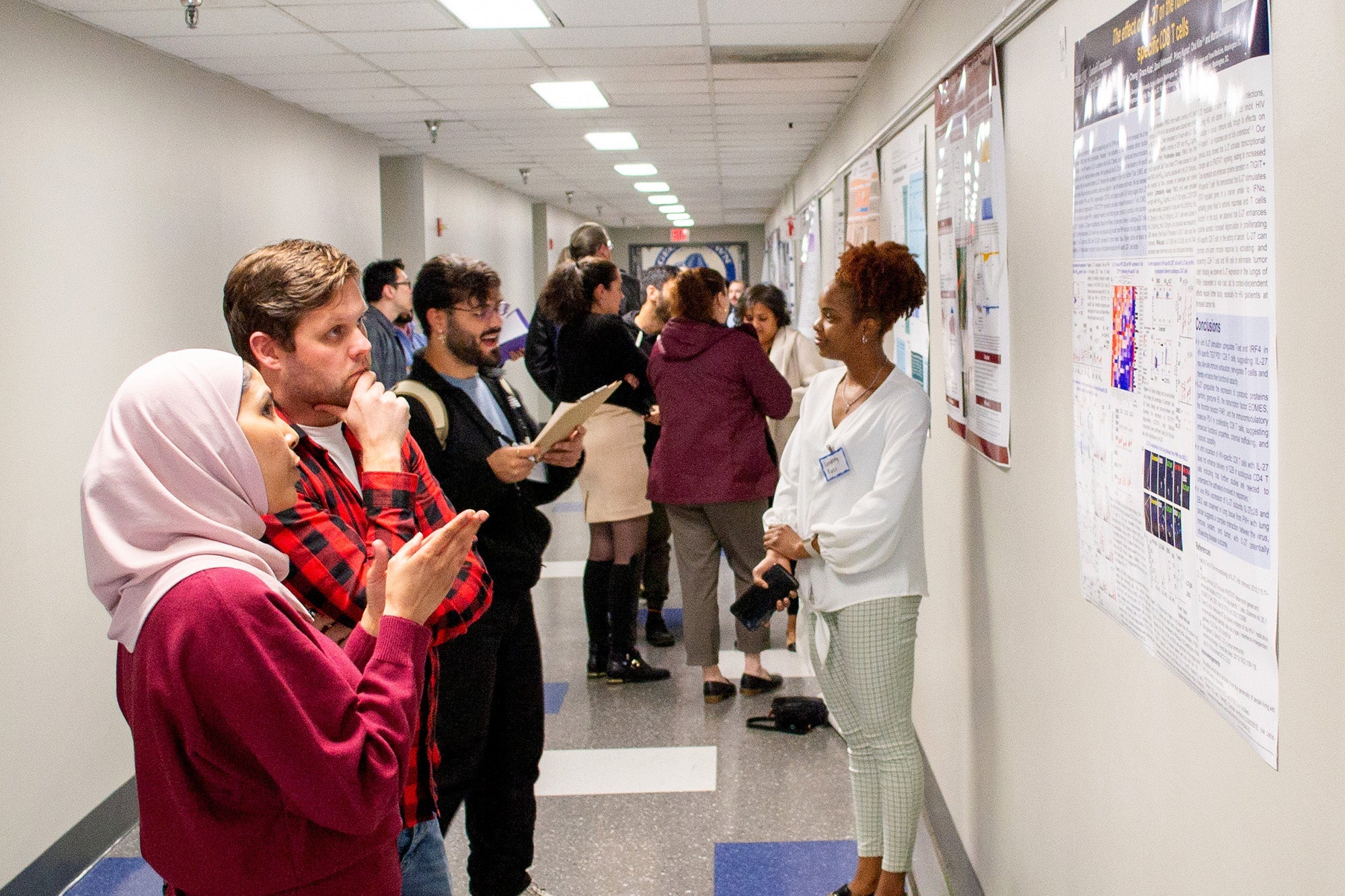 Students gather in a hallway to look at each other's research posters  on the walls