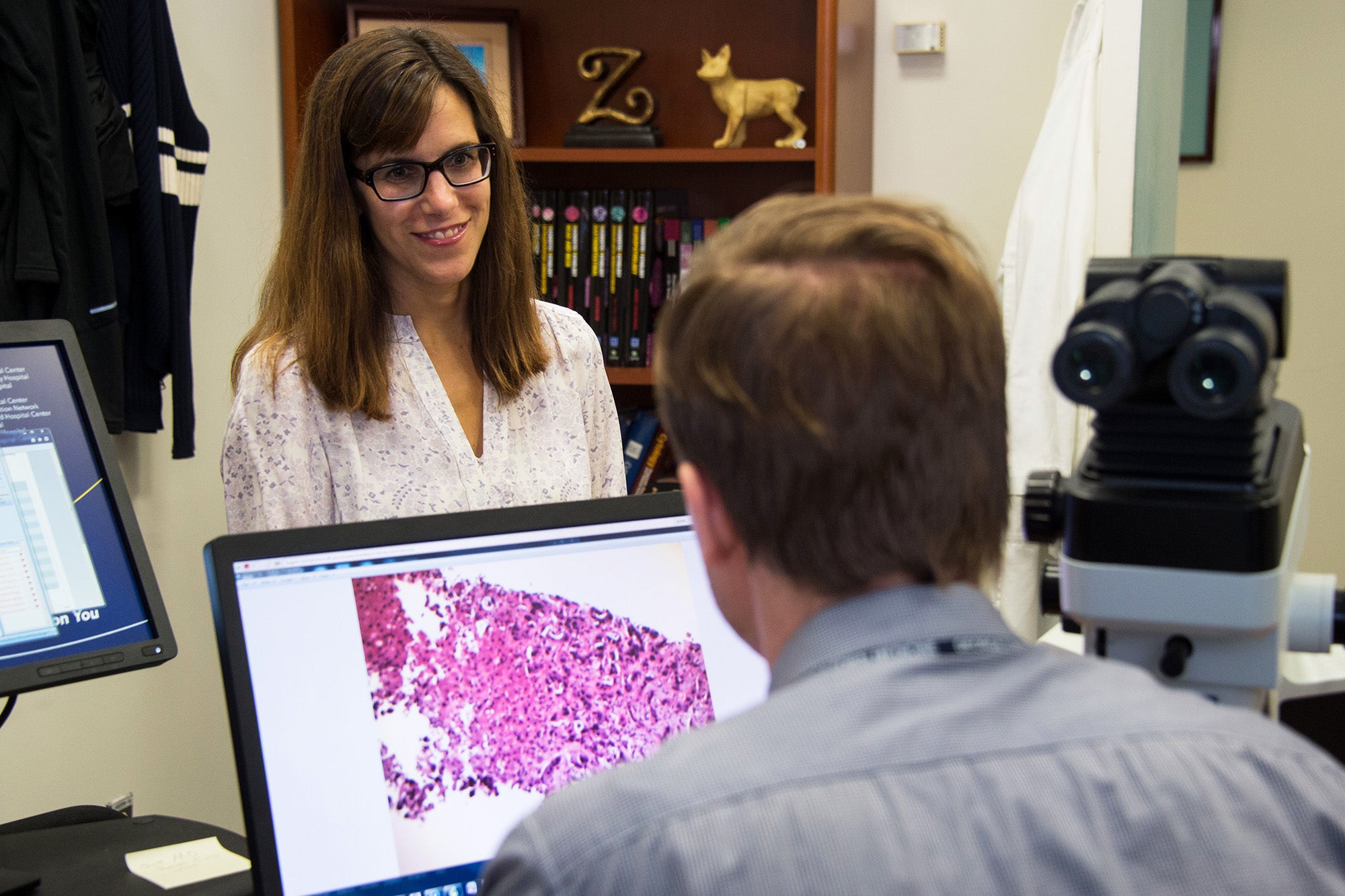 Mary Furlong speaks to a student working at a desk with computer displaying a microscope output