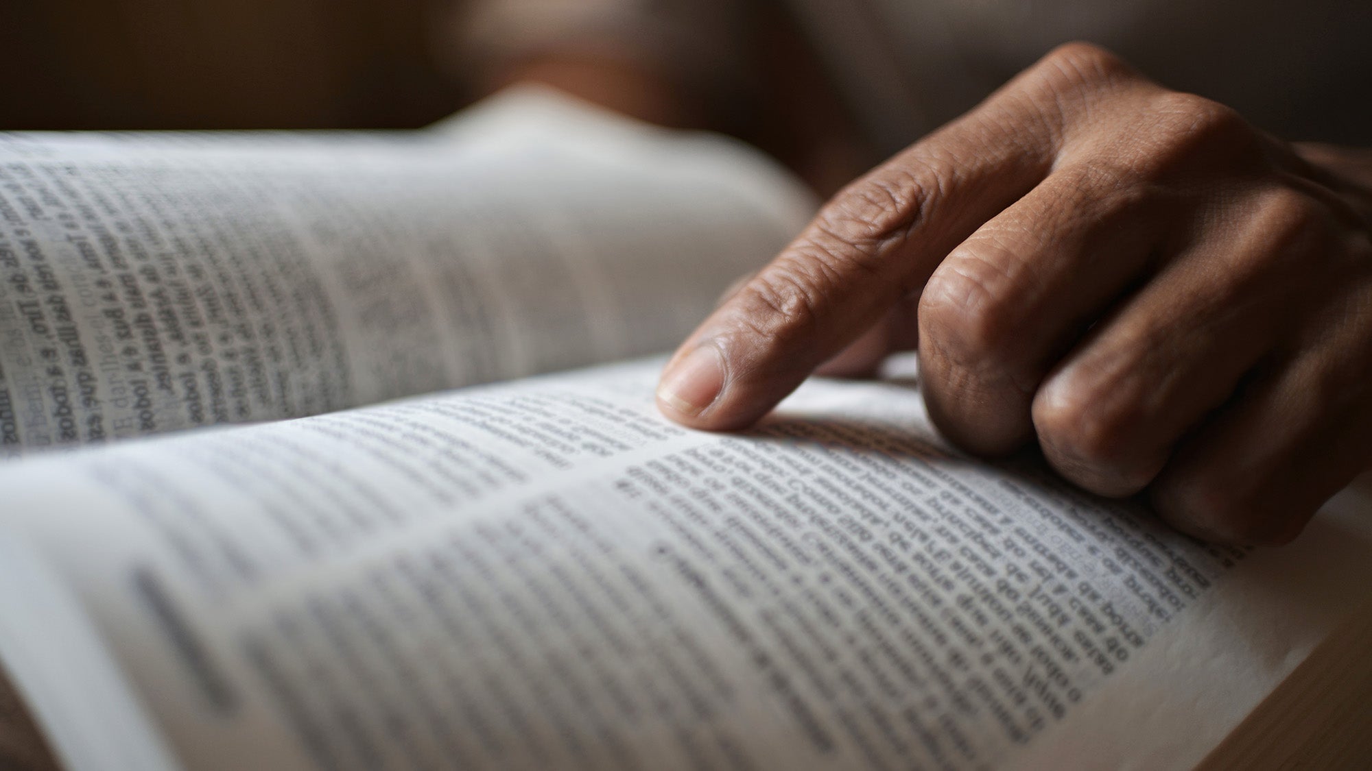 A person's hand points to words in a book