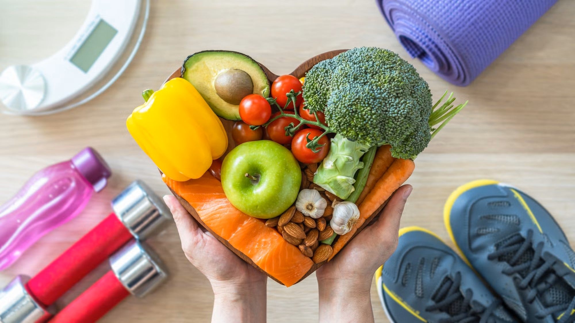 Fruits and veggies are packed in a heart shaped bowl with exercise equipment in the background