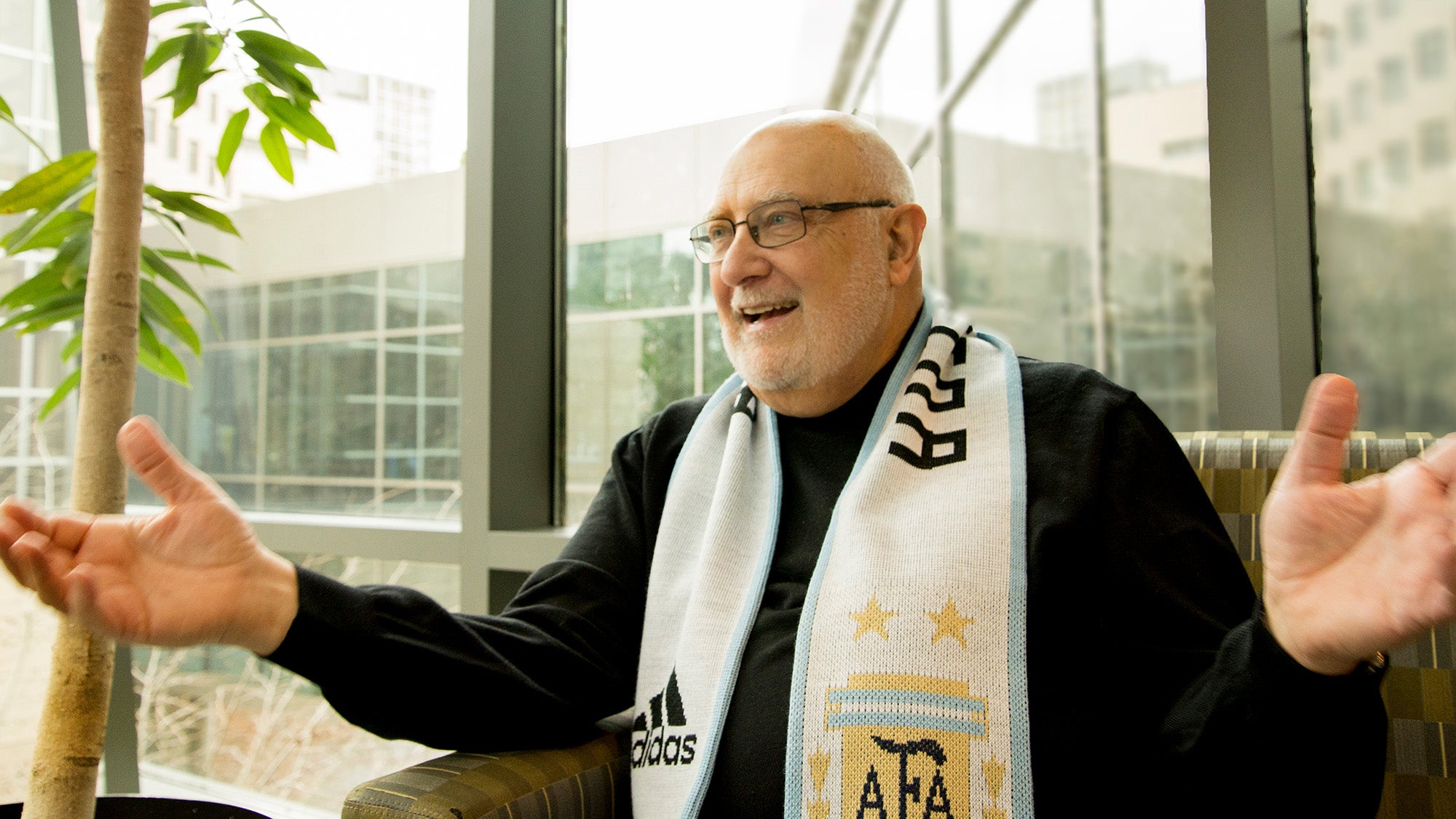 Dr. Pellegrini sits with arms outstretched wearing a scarf for his home soccer team in Argentina