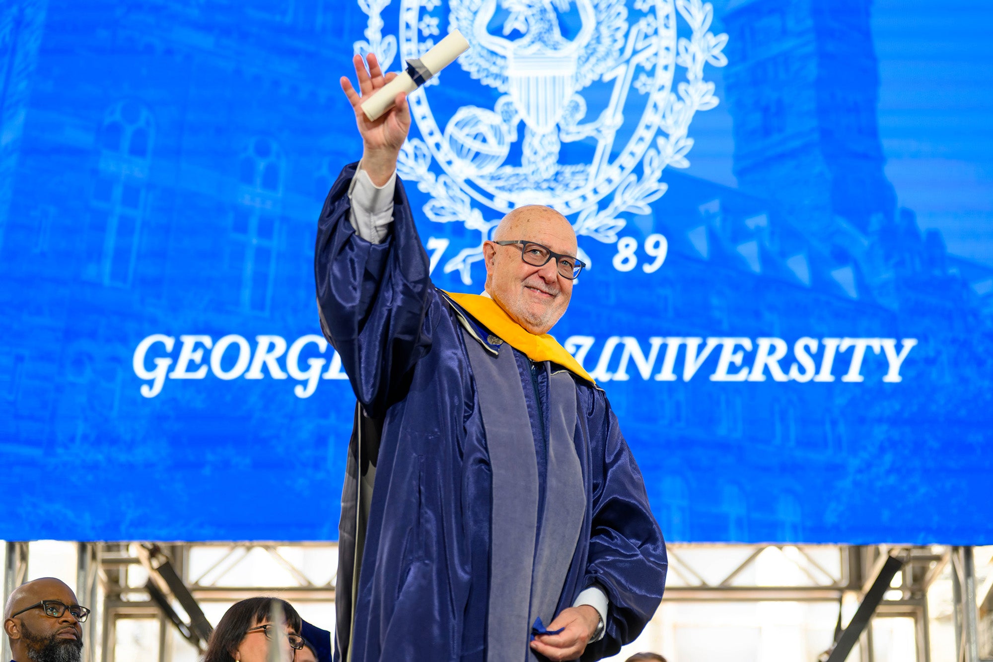 Carlos Pellegrini raises his hand grasping a rolled diploma