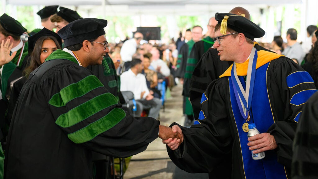 Two individuals in academic regalia shake hands