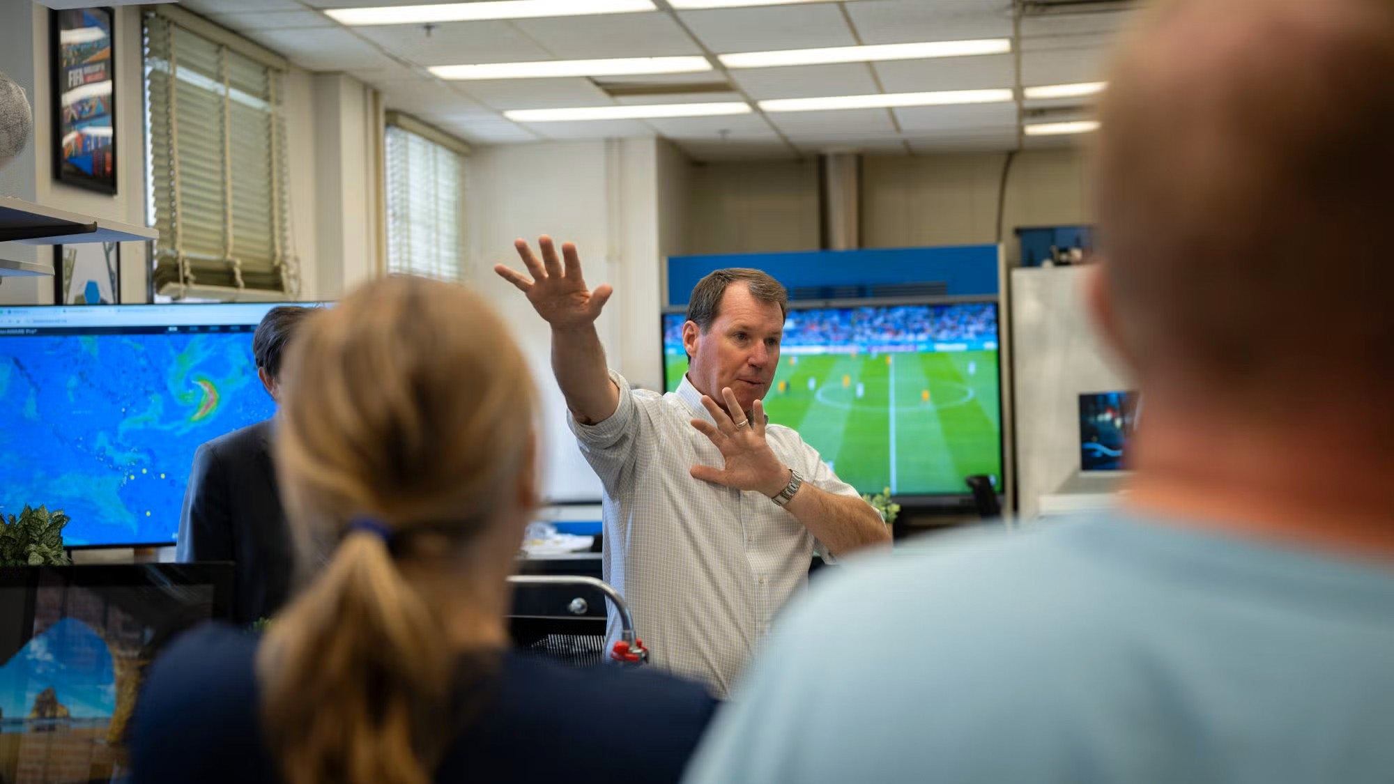 A man speaks to a group in a room filled with computer monitors