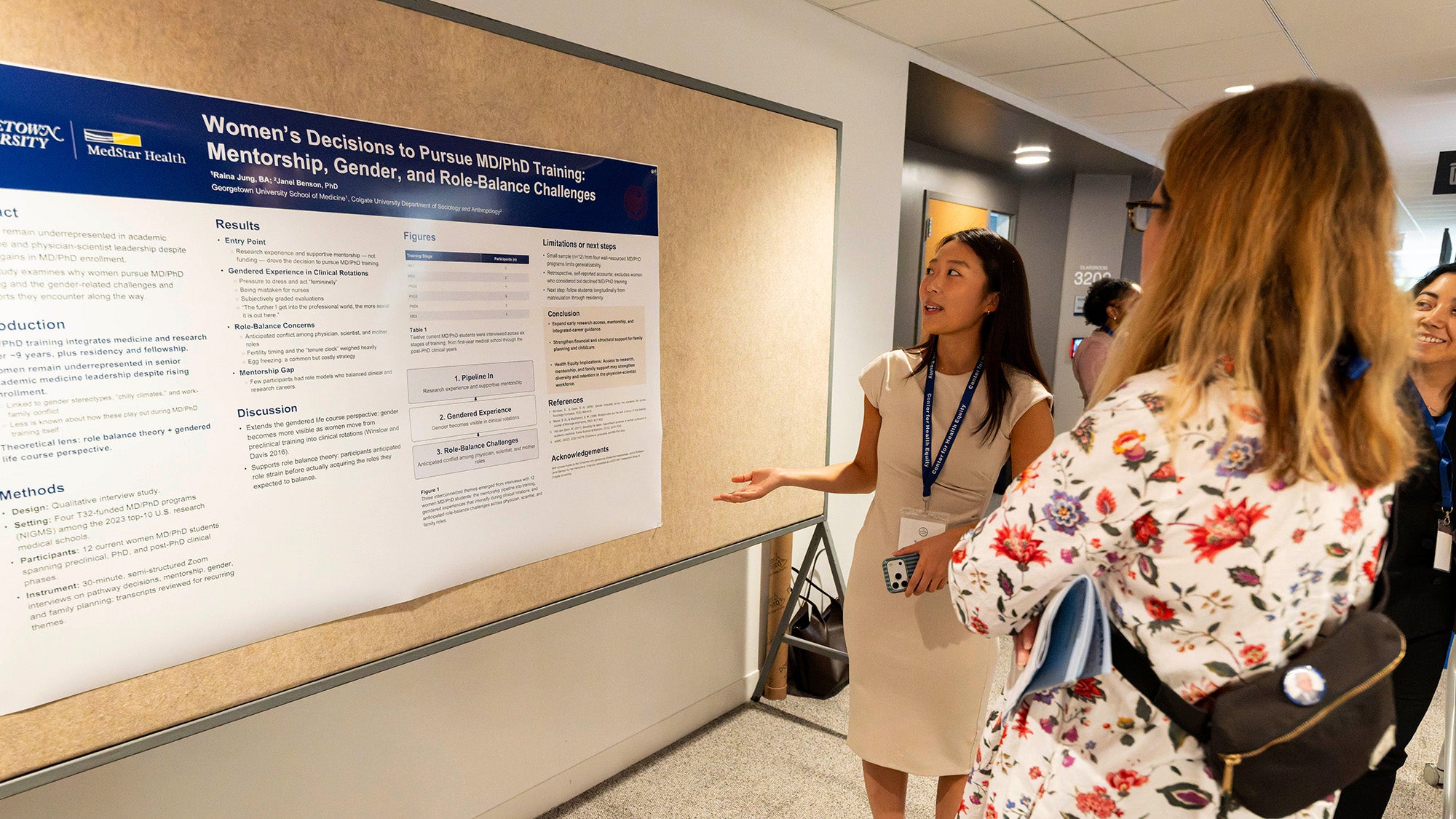 A female student presents her poster to other people during a poster session