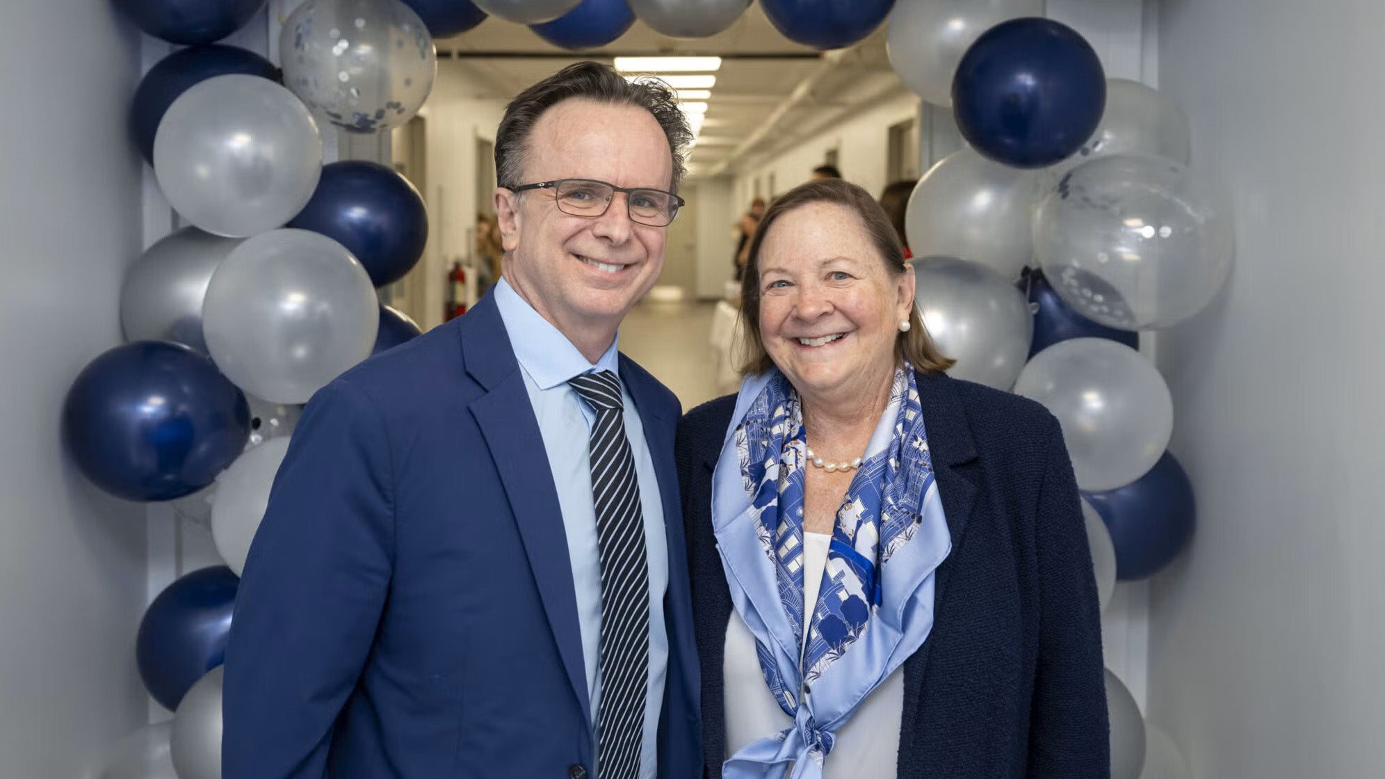 Dr. Beauchamp and Joan Ferrill stand in a hallway decorated with a balloon arch